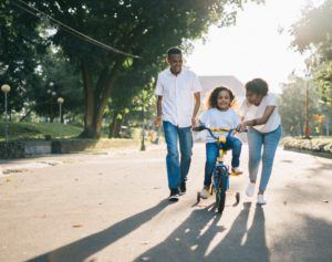parents showing affectin by teaching child to ride bicycle. physical activity is a good means of promoting mental health in children.